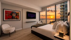 Una camera d'albergo moderna con un grande letto, una TV, un'opera d'arte incorniciata e vista sulla città.
