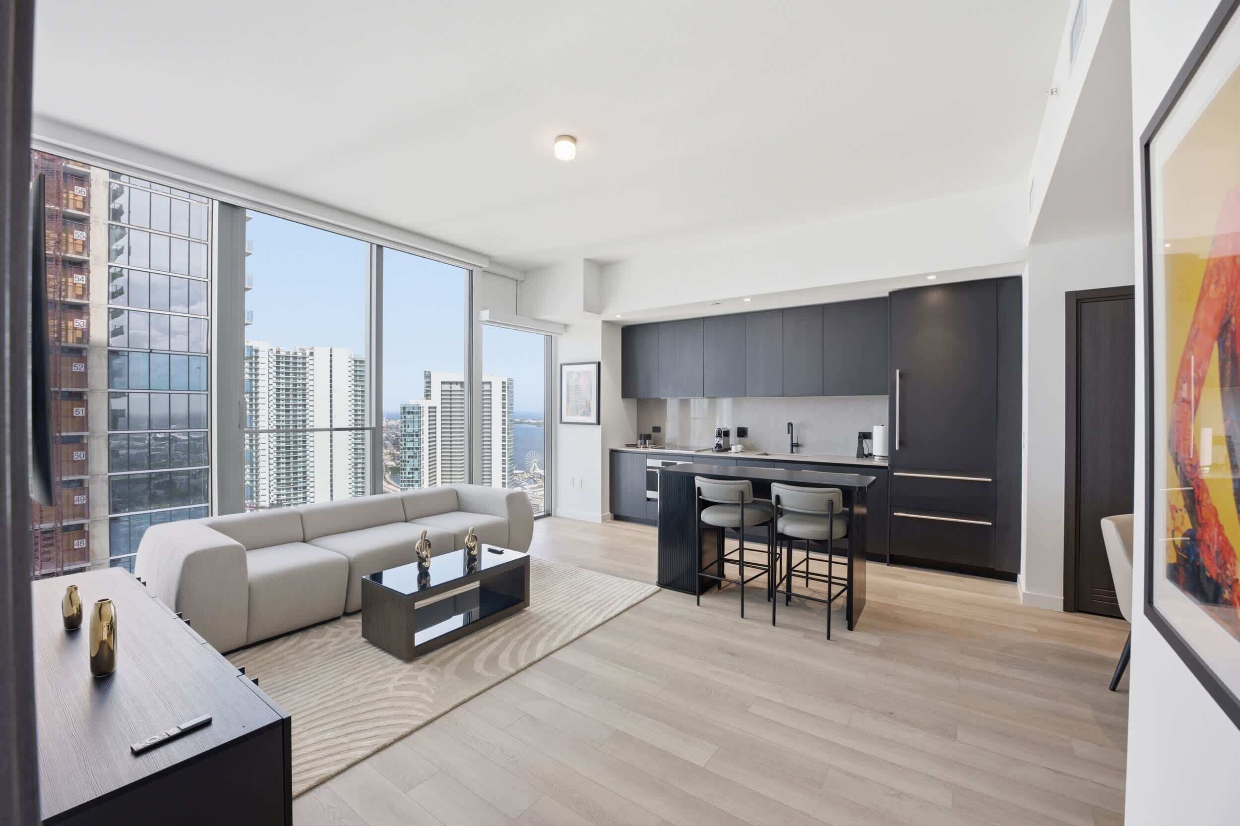 Eine moderne Wohnung mit Wohnzimmer, Küche und großen Fenstern mit Blick auf die Stadt.