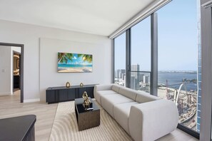 Ein modernes Wohnzimmer mit großem Fenster, einem Sofa, einem Couchtisch und einem Gemälde einer Strandansicht.