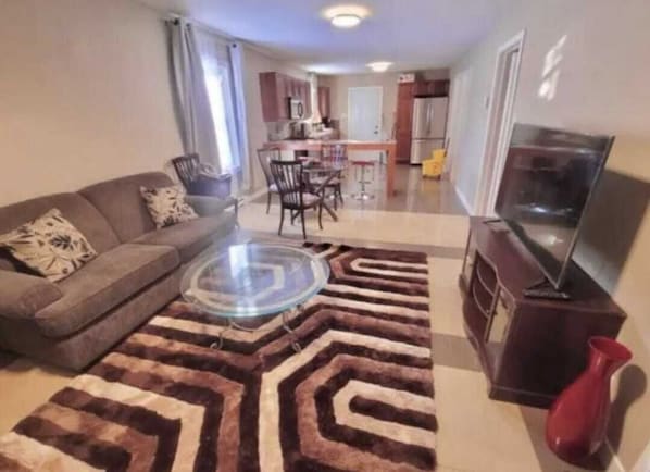 Un salon avec un canapé, une table basse, un téléviseur et, au fond, une cuisine.