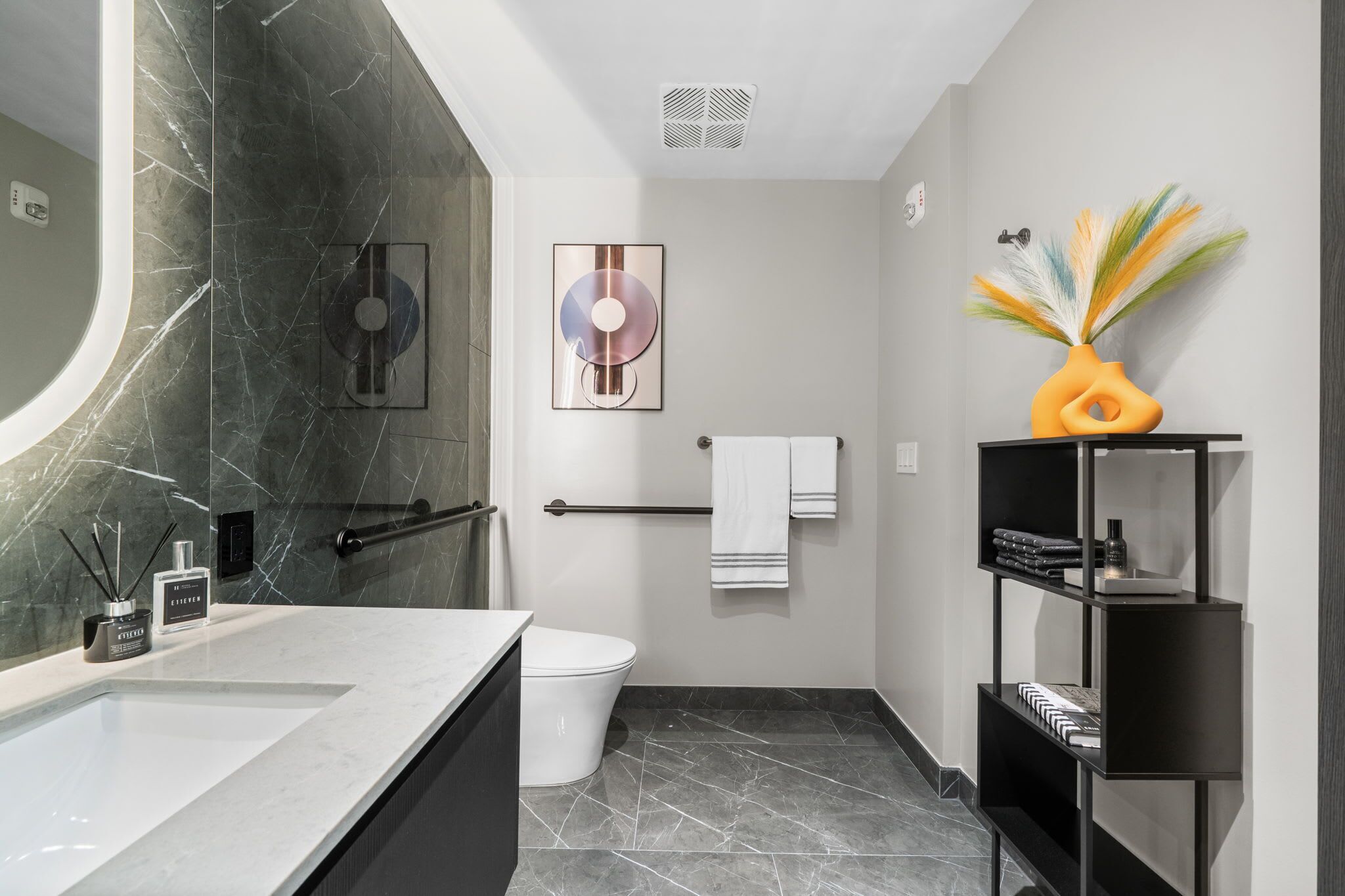Un baño moderno con lavamanos de mármol, inodoro, perchero y estante decorativo.