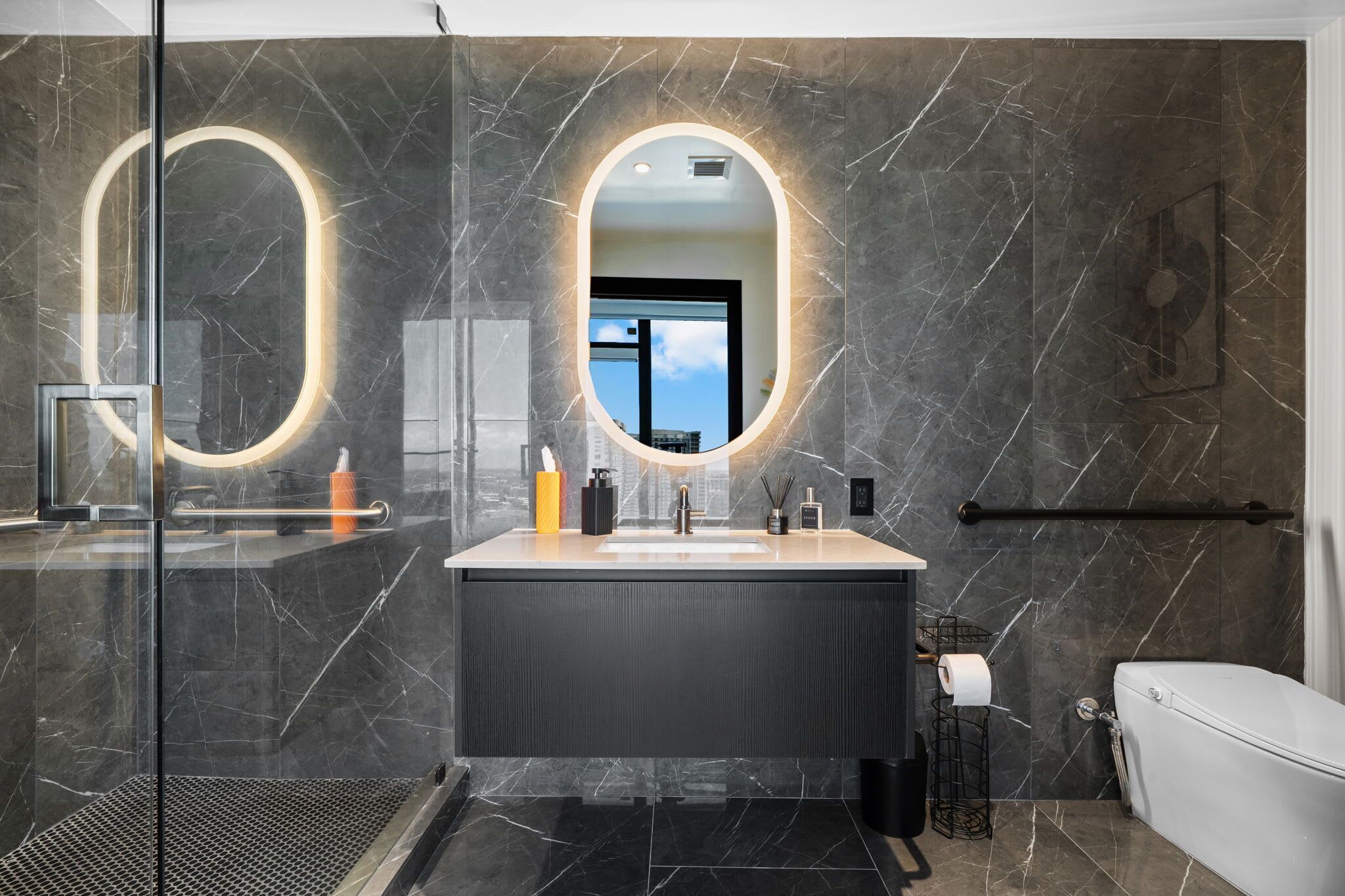Et moderne badeværelse med et stort spejl, marmorvægge og et toilet.