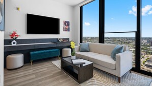 En moderne stue med stort TV, sofa, sofabord og udsigt over byen gennem store vinduer.