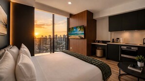 Une chambre d’hôtel moderne dotée d’un grand lit, offrant une vue sur la ville, et comprenant une kitchenette et un coin repas.