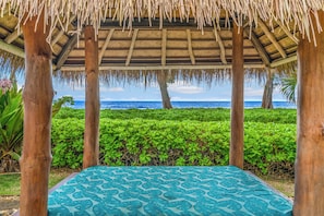 A covered outdoor seating area with a patterned blue cushion, wooden pillars, and a view of the ocean.