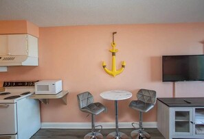 A kitchen with a microwave, stove, and a TV on a cabinet. There are two bar stools and a round table. - Sea Mist 50810 Ocean View Escape (Myrtle Beach)