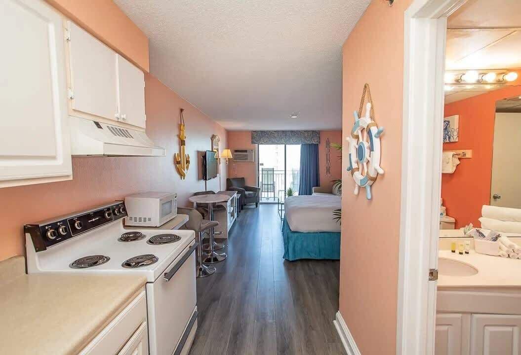 Une chambre d’hôtel compacte comprenant un coin cuisine, un lit, un petit espace repas et une salle de bain.