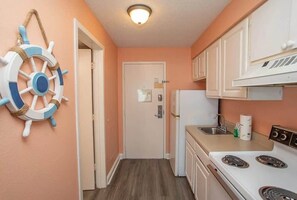 A compact kitchen with white cabinets, a stove, a sink, and a door with a small window. - Sea Mist 50810 Ocean View Escape (Myrtle Beach)