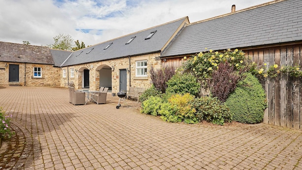 A stone building with a tiled patio, outdoor seating, and a wooden fence. - Host & Stay | The Spinney (Consett)