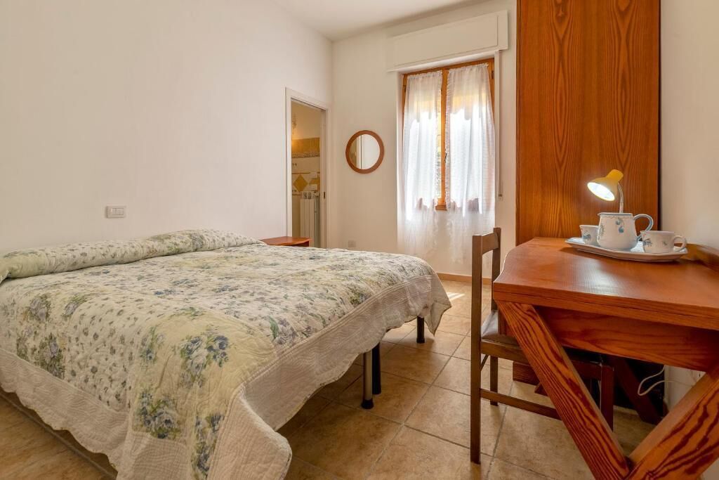 A bedroom with a bed, a wooden table with a lamp, and a window with curtains.