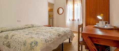 A bedroom with a bed, a wooden table with a lamp, and a window with curtains.