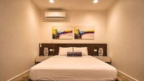 Une chambre d’hôtel avec un grand lit, deux climatiseurs fixés au mur et deux tableaux abstraits.
