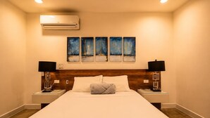Une chambre d’hôtel avec un grand lit, deux tables de chevet avec des lampes, un climatiseur et quatre tableaux abstraits accrochés au mur.
