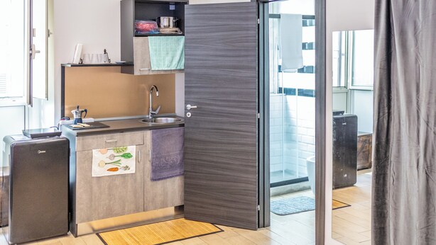 Una cocina compacta con refrigerador, lavamanos y un mueble pequeño.