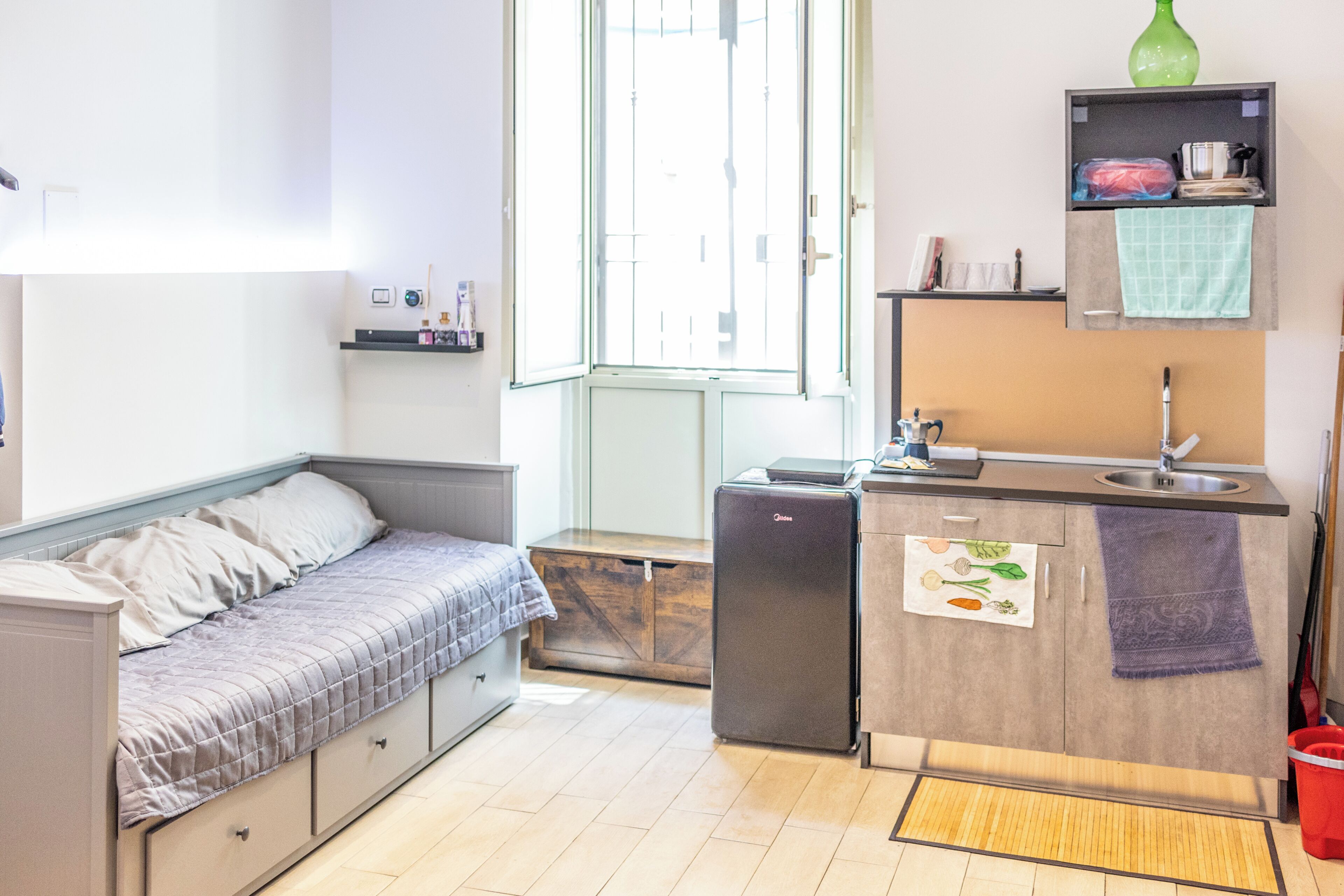 Una habitación pequeña con cama, kitchenette y ventana.