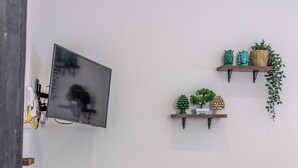 Un comedor con una mesa, sillas, un televisor montado en la pared y estantes decorativos con plantas.