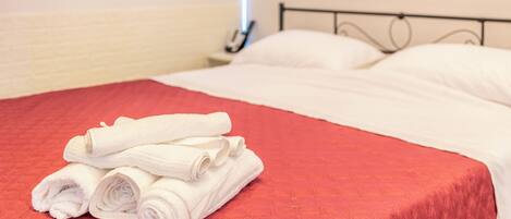 Una cama bien hecha con sábanas blancas y una colcha acolchada roja.
