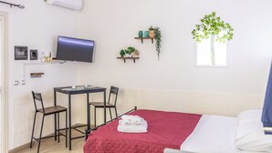 Una habitación de hotel con cama, escritorio con silla, televisor y estantes empotrados con plantas.