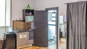Una cocina compacta con refrigerador, pileta y un estante con un florero verde.