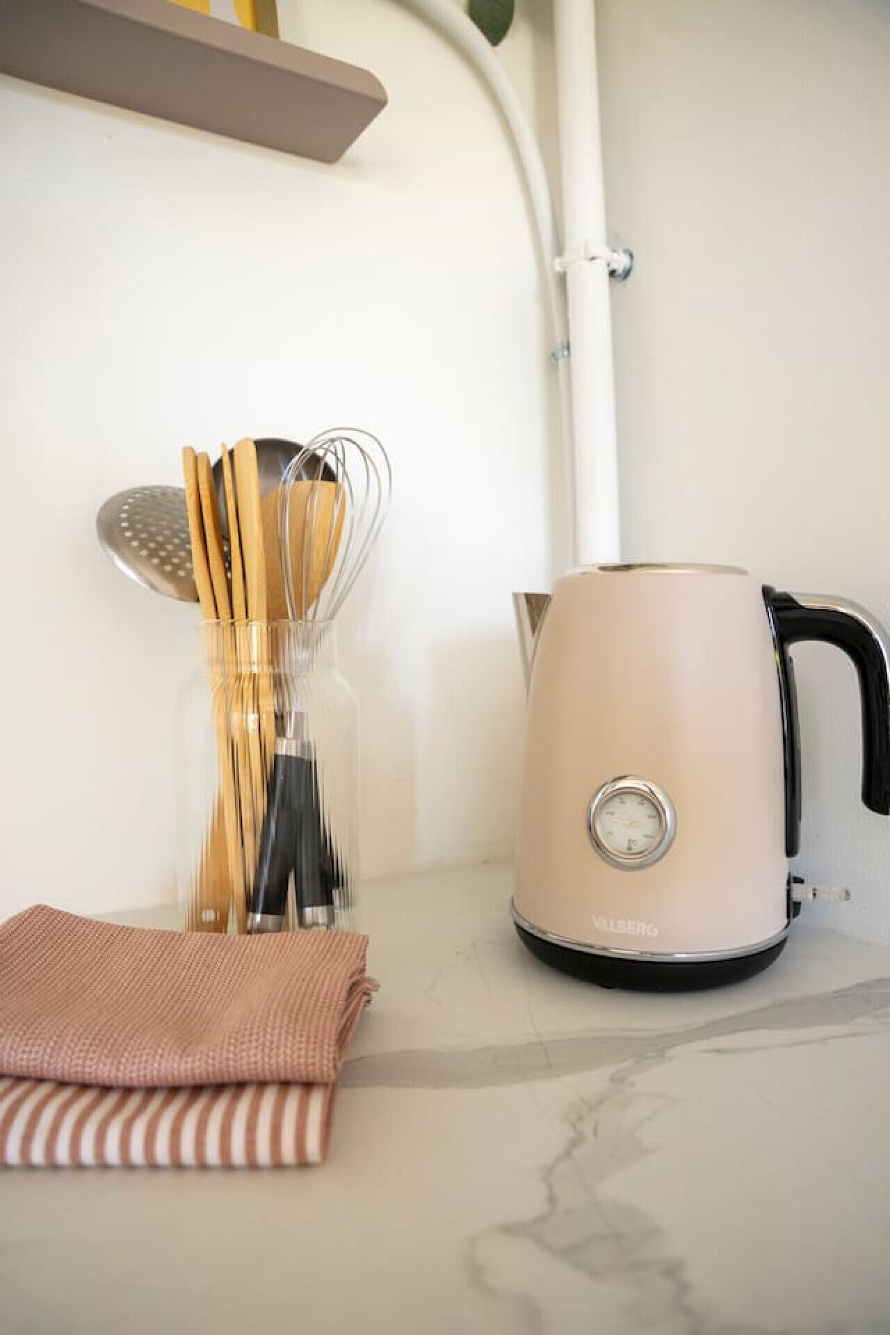 A kitchen counter with a kettle, a colander, wooden utensils, and a folded cloth.