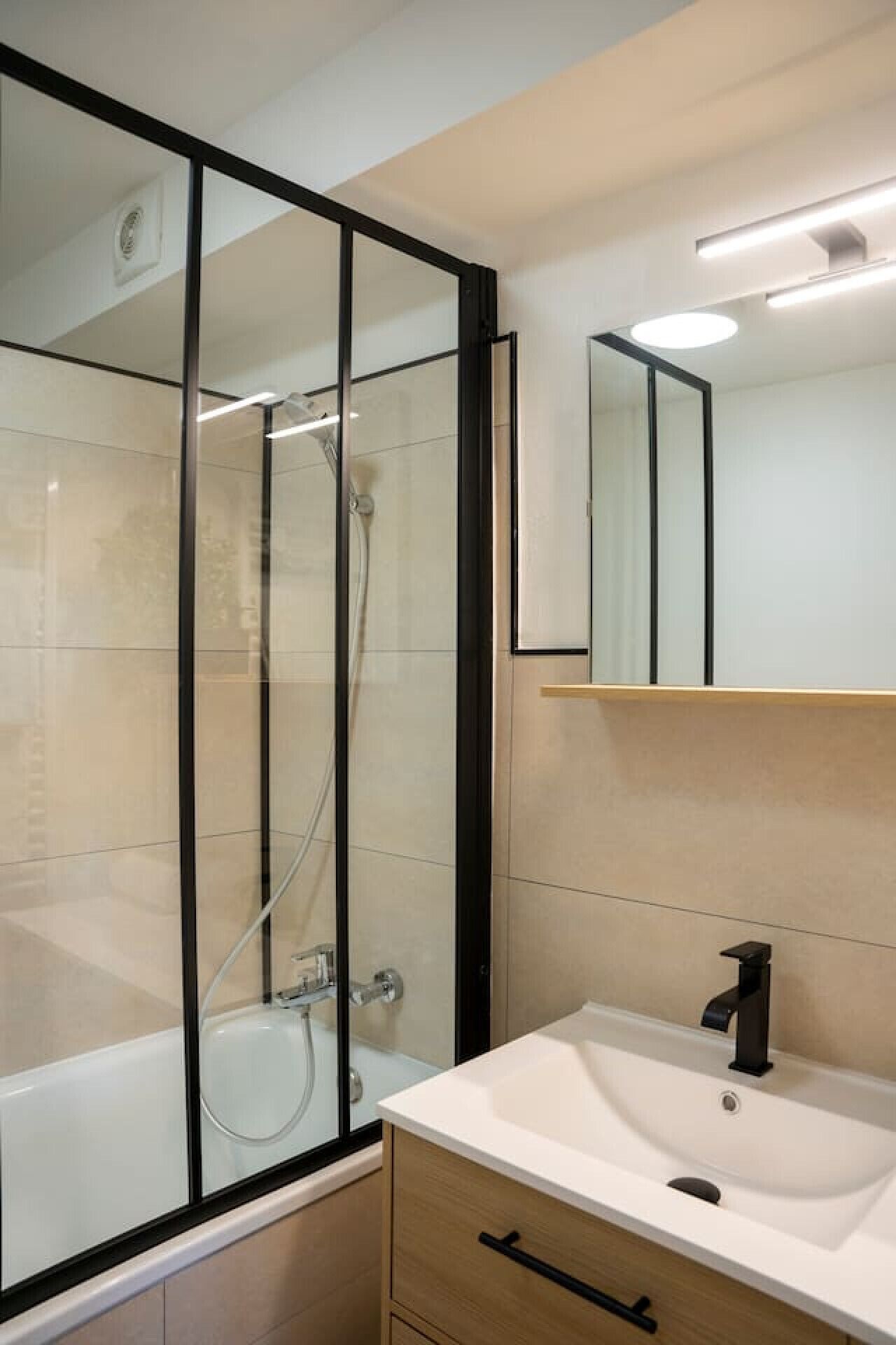 Ein modernes Badezimmer mit einer gläsernen Duschkabine, einem weißen Waschbecken und einem Spiegel darüber.