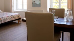 Una habitació amb un llit, una taula de menjador amb cadires, un mirall i finestres grans.