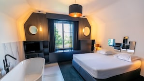 Ein modernes Hotelzimmer mit einem großen Bett, einer Badewanne, einem Fernseher und einem Fenster mit Vorhängen.