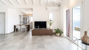 A spacious living area with a flat-screen TV, a dining table with chairs, and a large window offering a view.
