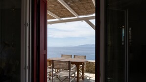An open door leading to a patio with a table and chairs, overlooking a body of water and distant mountains.