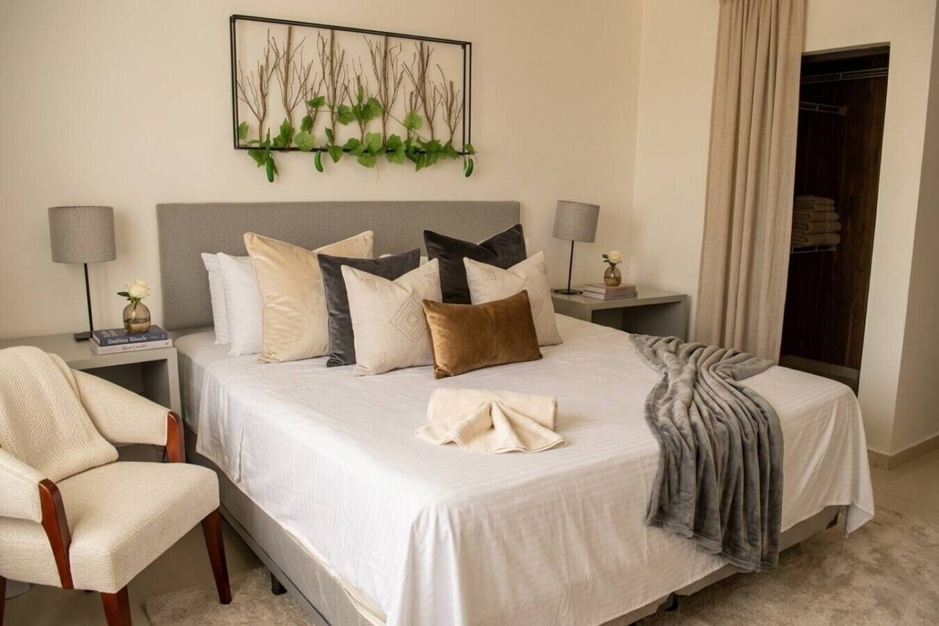 Quarto de hotel bem organizado com uma cama, uma cadeira, uma mesa de cabeceira com abajur e uma obra de arte na parede.