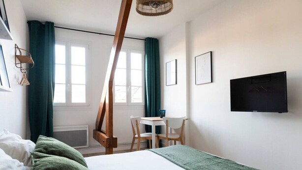 Une chambre à coucher avec un lit, un bureau, une chaise, une télévision et une fenêtre avec des rideaux.