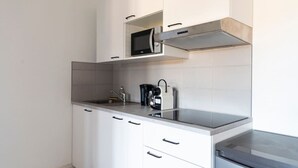 Une cuisine moderne avec des meubles blancs, un évier en acier inoxydable, un four à micro-ondes et une machine à café.