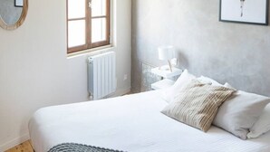A bedroom with a large bed, a hanging light fixture, a window, and a framed picture on the wall. - Apartment for 2, Place St. Sauveur (Caen)