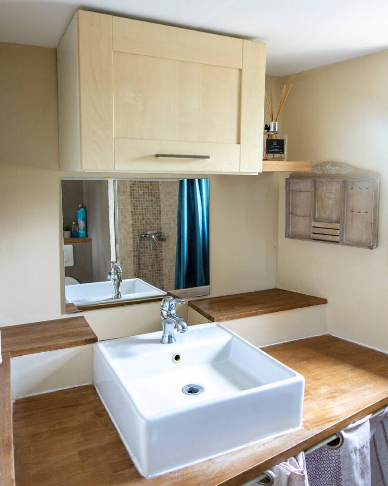 Une salle de bain avec un lavabo blanc, un plan de toilette en bois, un miroir et un meuble au-dessus du lavabo.
