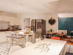 Cocina moderna con muebles blancos, refrigerador de acero inoxidable y zona de comedor con mesa y sillas blancas.