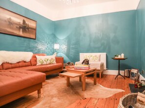 Ein gemütliches Wohnzimmer mit einer türkisblauen Wand, einem weichen orangefarbenen Sofa, einem Holztisch und einem weißen Heizkörper.
