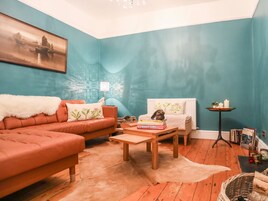 Un salon chaleureux avec un mur de couleur turquoise, un canapé orange moelleux, une table basse en bois et un radiateur blanc.