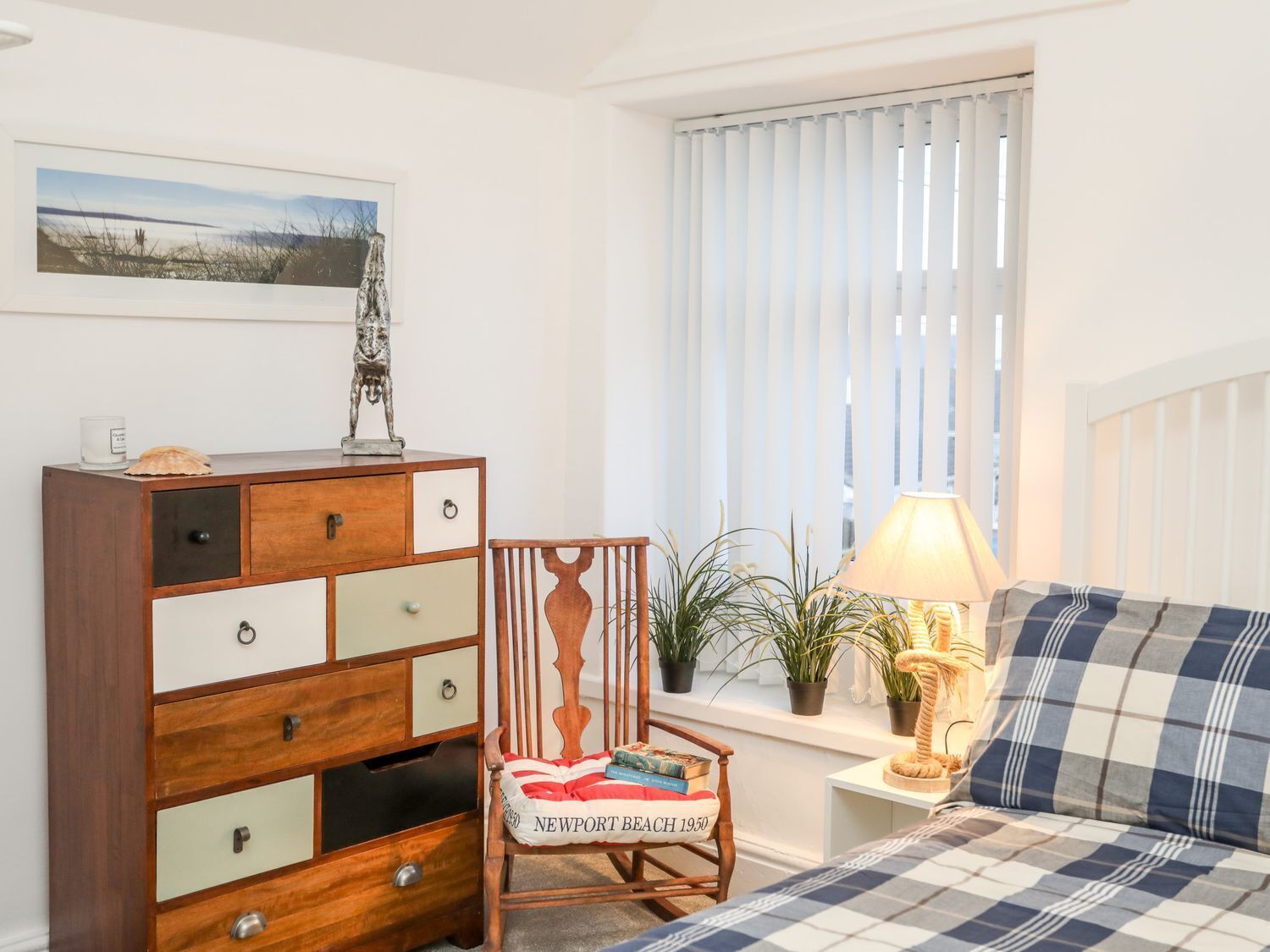 A bedroom with a bed, a dresser, a chair, a window with blinds, a lamp, and a framed picture on the wall.