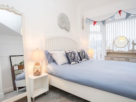 Un dormitorio con cama, mesitas de noche, cómoda, espejo y ventana con persianas.