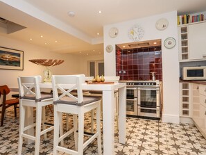 A modern kitchen with a dining area, featuring a white table, chairs, a stove, oven, and a microwave. - Rhiwlas (Rhosneigr)