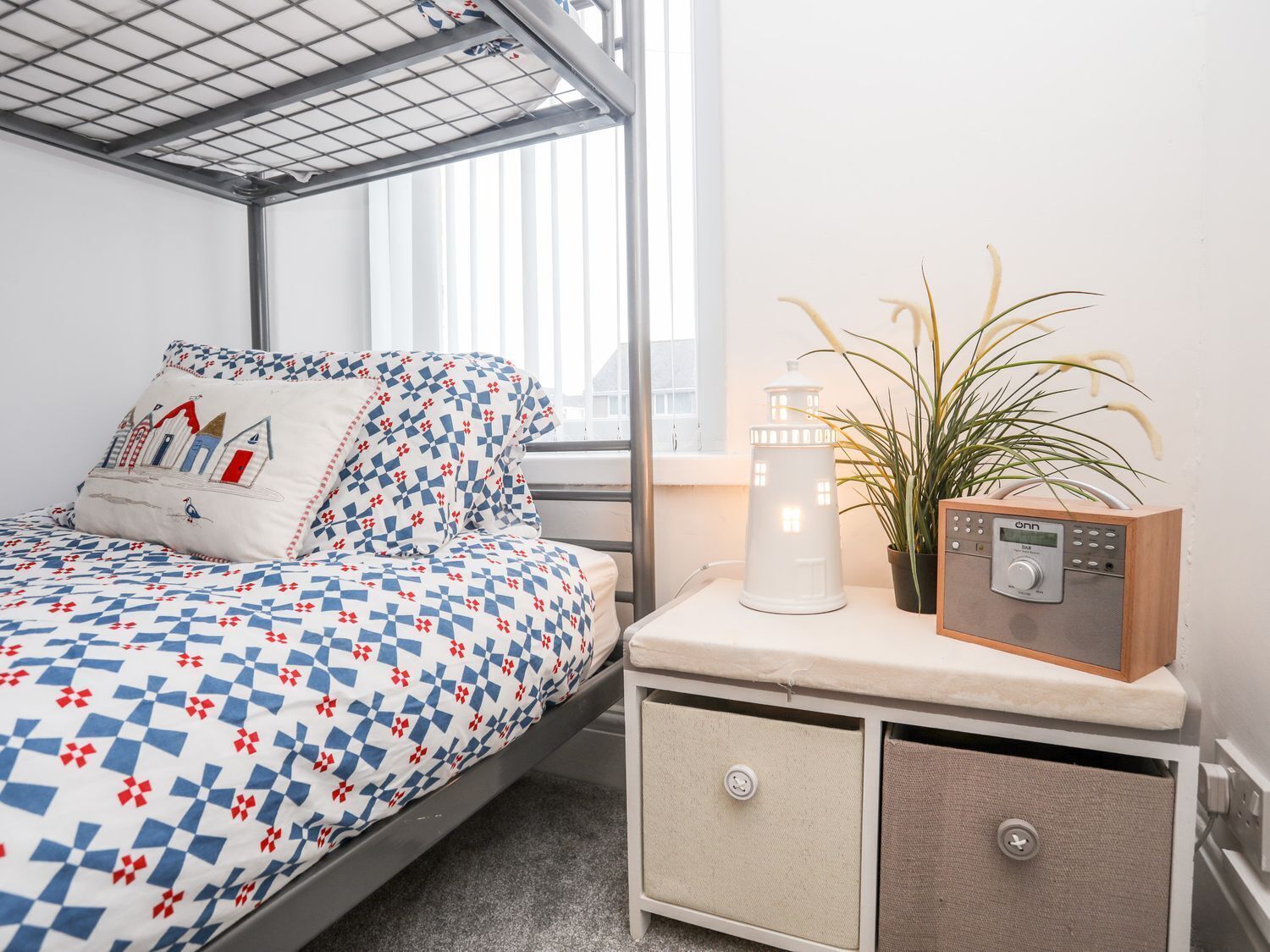 Un dormitorio con cama, mesita de noche con radio, planta en maceta y ventana.