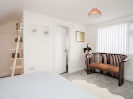 Un dormitorio con cama, una escalera de madera, sofá, lámpara colgante y ventana con persianas.