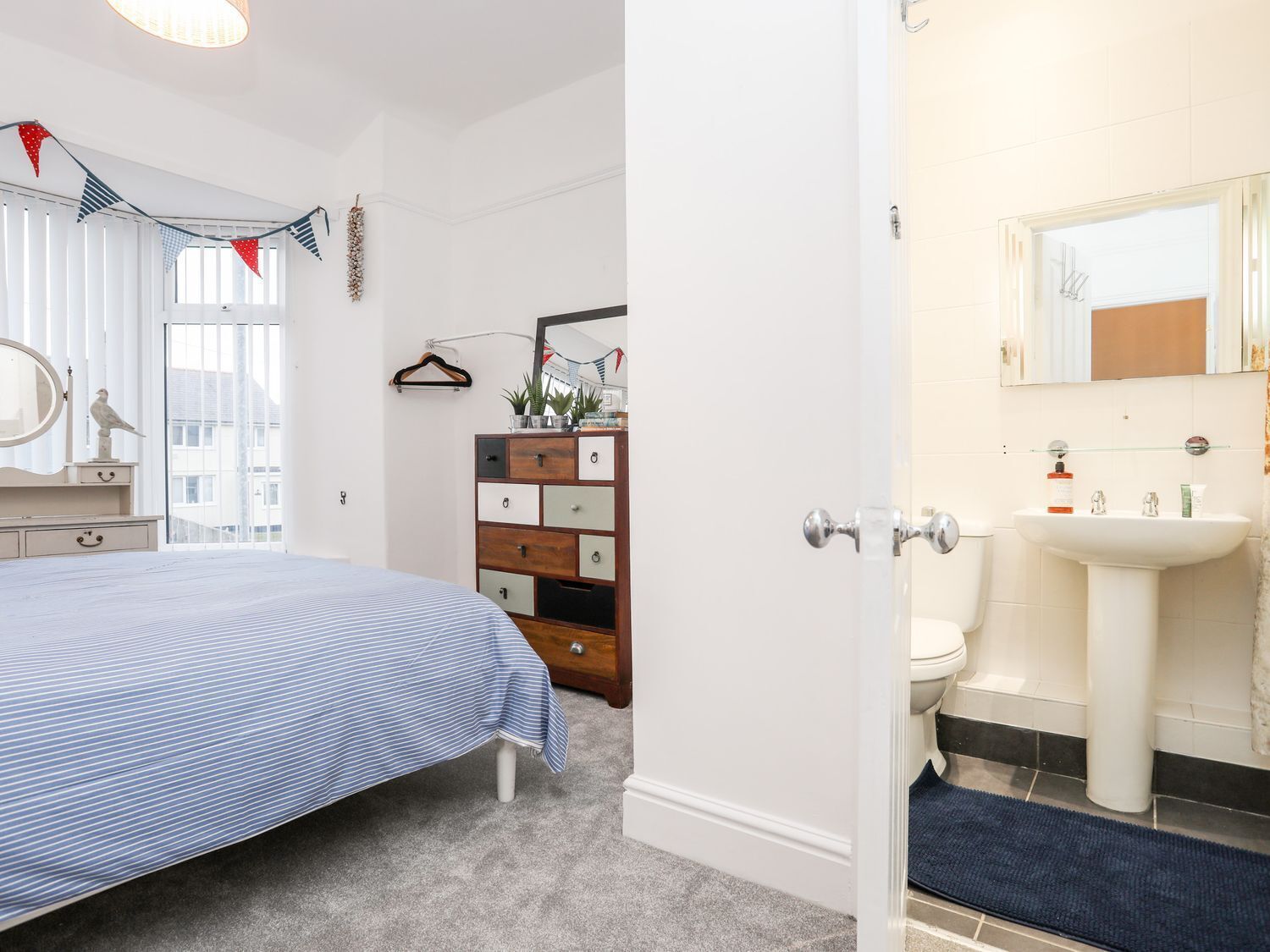 A bedroom with a bed, dresser, and a bathroom with a sink and toilet.