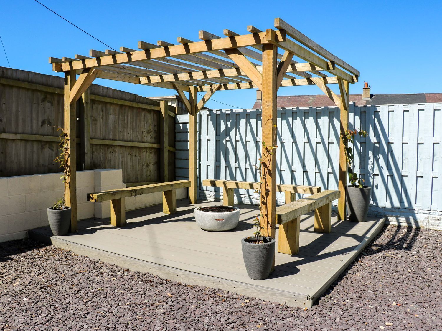 Una estructura de pérgola de madera con bancos y plantas en macetas.