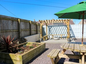 A wooden deck with a pergola, a raised garden bed with plants, and a picnic table with an umbrella. - Rhiwlas (Rhosneigr)