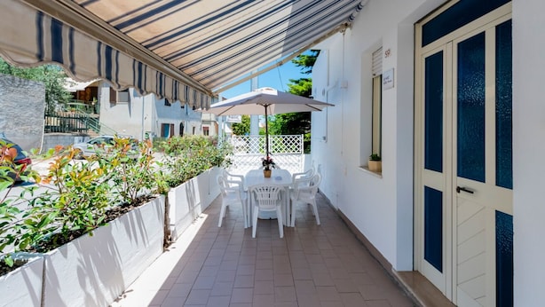 A covered outdoor seating area with a table and chairs, a white door, and a window. - A charming 90-square-meter villa, perfect for six guests, featuring a private street-level entrance.The property is situated in a quiet area of ​​Silvi and enjoys a great location: thanks to a pedestrian path, you can reach the sea in just 10 minutes (Silvi)