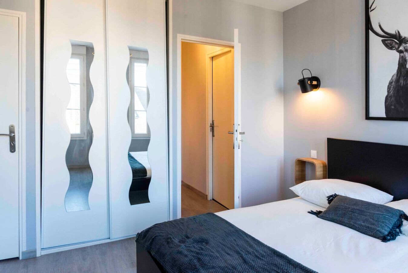 Una camera da letto con un letto, una lampada a parete, un quadro raffigurante un cervo e un design di porta originale.