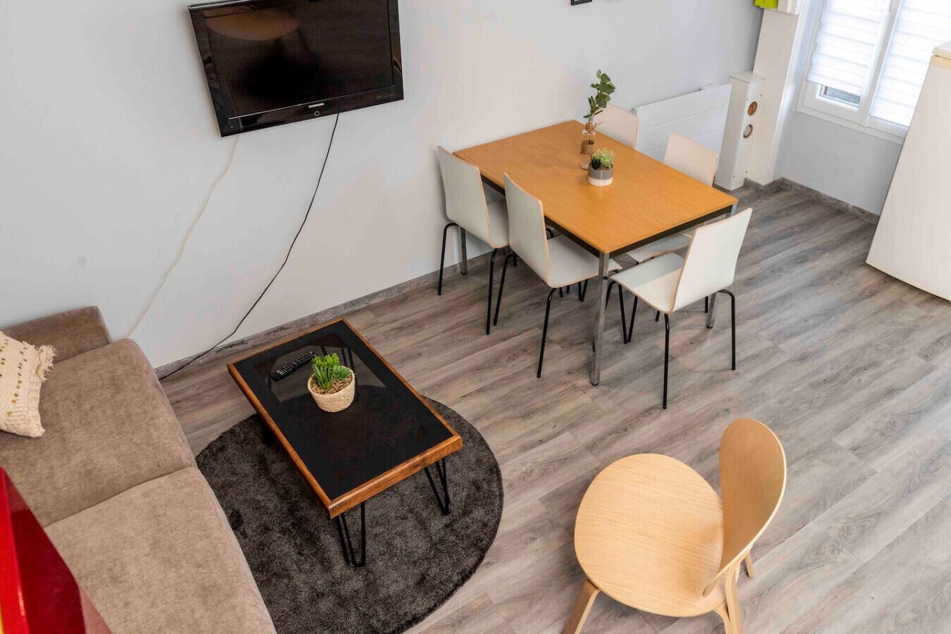 Un salon moderne comprenant un canapé, une table basse, une table à manger avec des chaises, un téléviseur fixé au mur et une petite plante en pot.