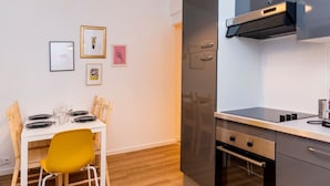 Een kleine keuken met een inbouwoven, een eettafel met stoelen en kunstwerken in lijsten aan de muur.