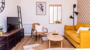 Een woonkamer met een televisie, een bank, een stoel, een tafel en een wandklok.